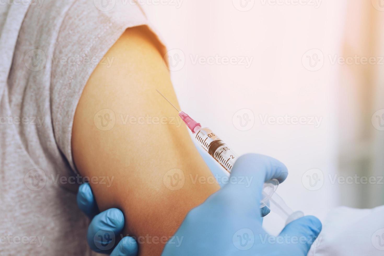 close up doctor holding syringe and using cotton before make injection dose in shoulder of patient in medical mask. Covid-19 or coronavirus vaccine. prevention against flu or virus pandemic concept. photo