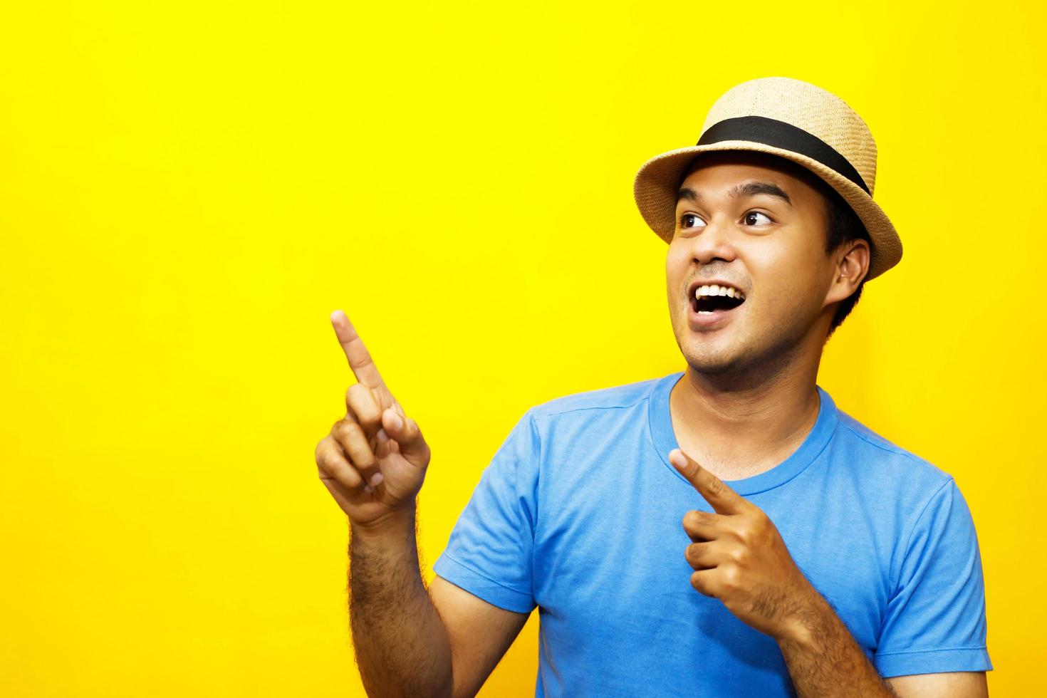 Portrait of cheerful asian man in basic clothing Casual wear hat smiling and show giving thumbs up at camera with showing success. isolated over yellow background. photo