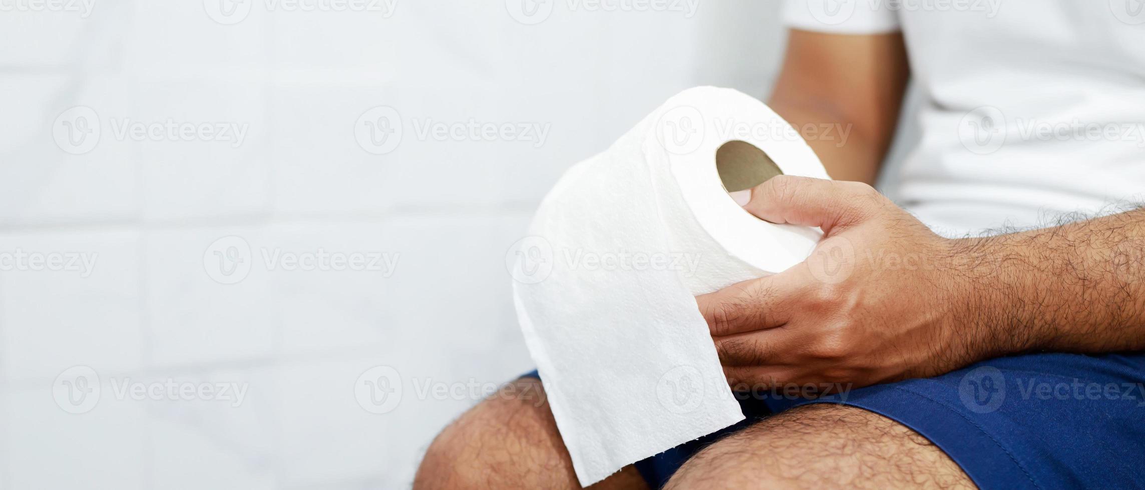 Man suffers from diarrhea hand hold tissue paper roll in front of toilet bowl. constipation in bathroom. Treatment stomach pain and Hygiene, health care photo