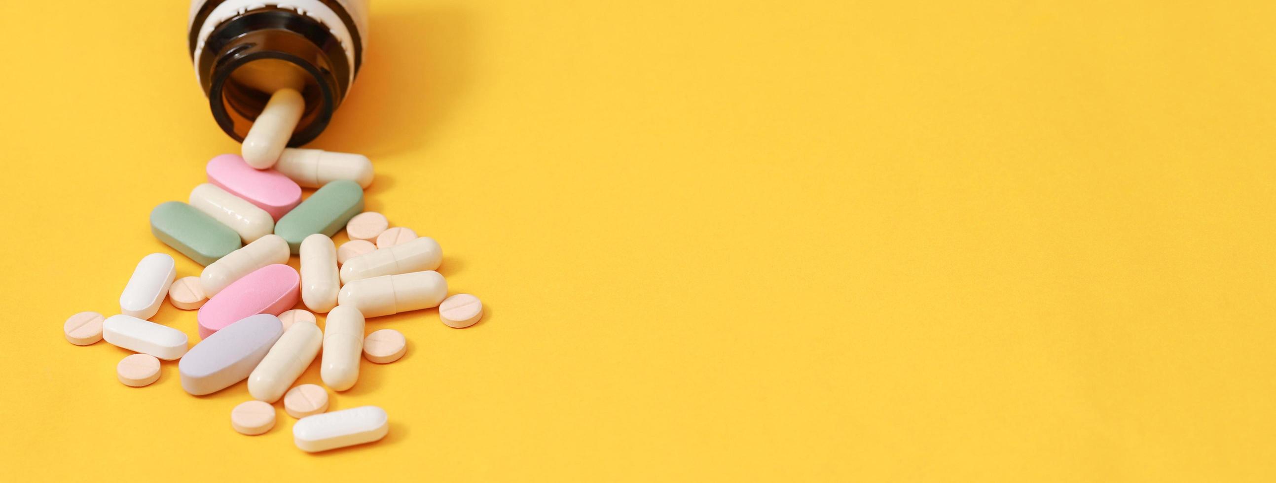 Pill bottle spilling out. colorful pills on to surface tablets on yellow background. top view. drug medical healthcare concept photo