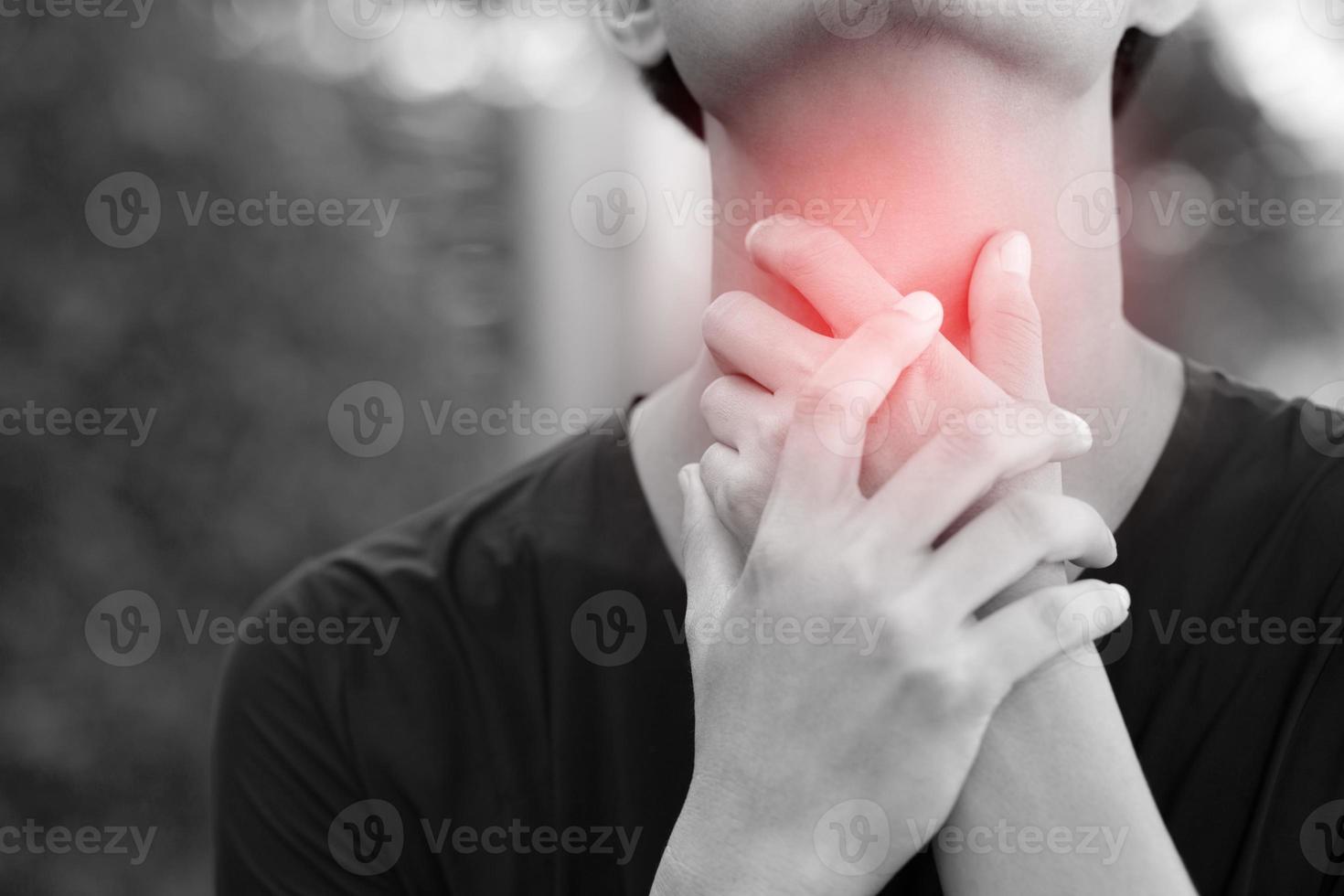 sore throat pain. Closeup of young man sick holding her inflamed throat using hands to touch the ill neck in blue shirt on gray background. Medical and healthcare concept. Focus red on to show pain. photo