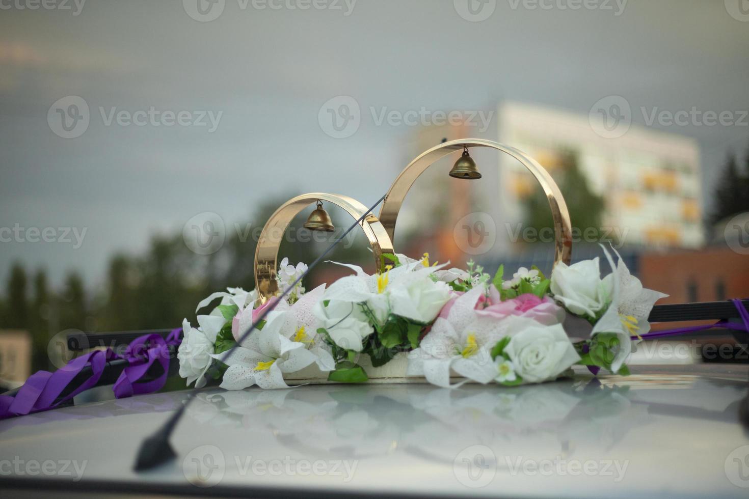 Wedding rings on roof of car. White flowers and bells adorn newlyweds' car. photo