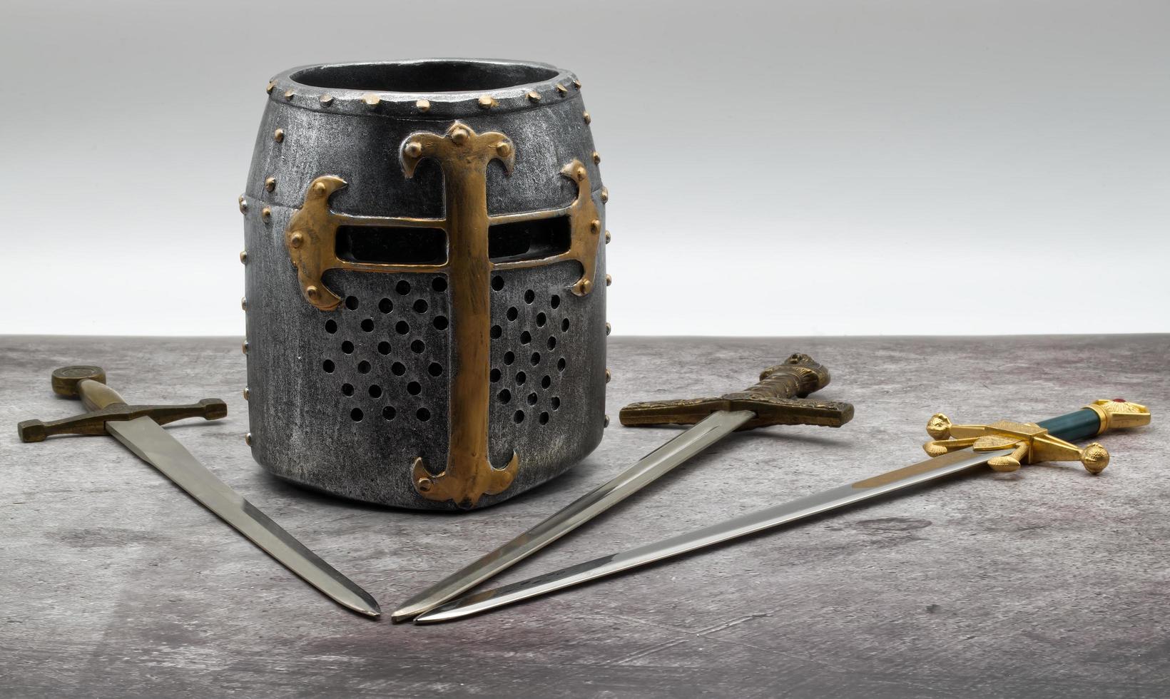 casco de caballero medieval y espadas aisladas en una mesa de piedra. foto