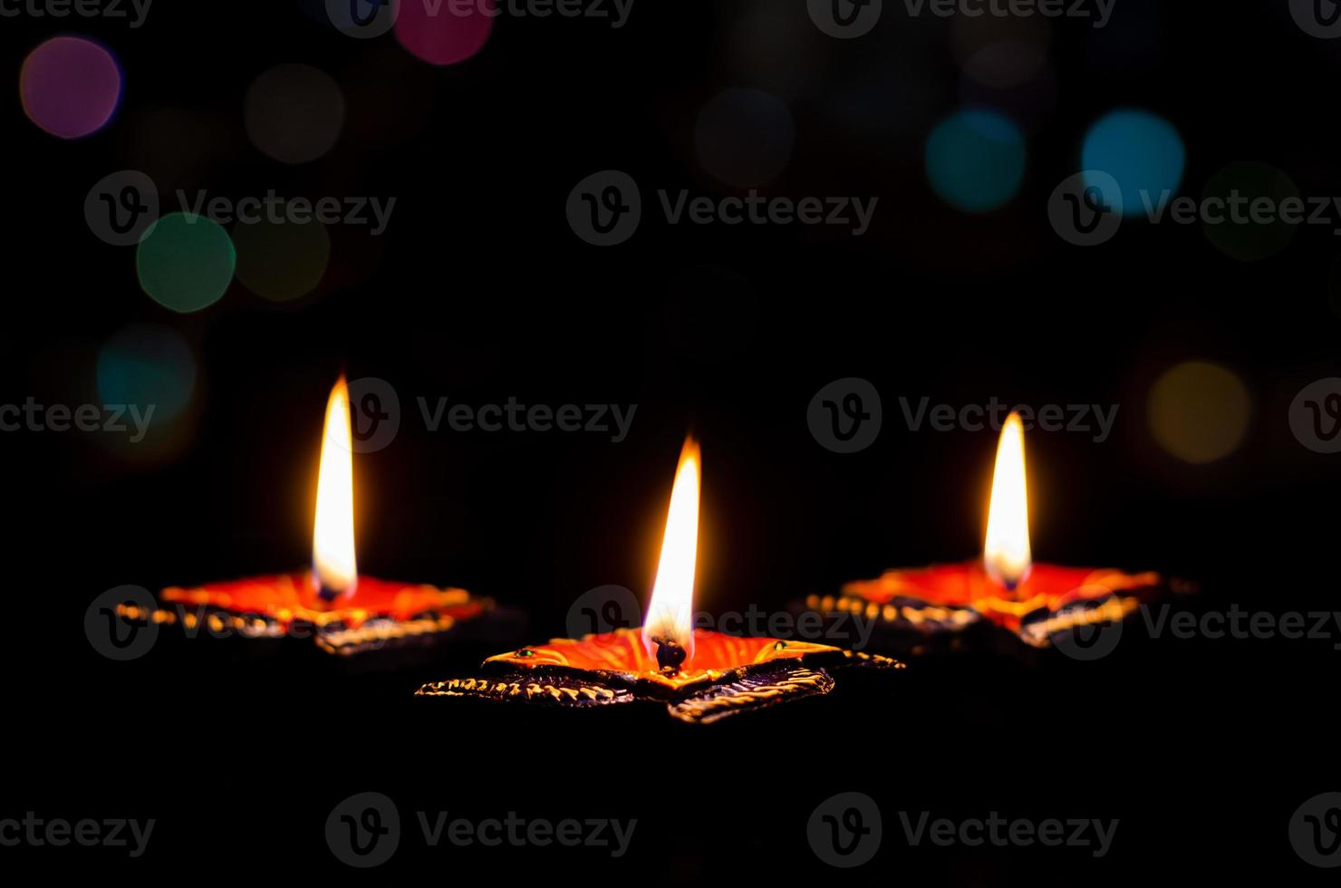 Selective focus on flame of clay diya lamps lit on dark background with colorful bokeh lights. Diwali festival concept. photo