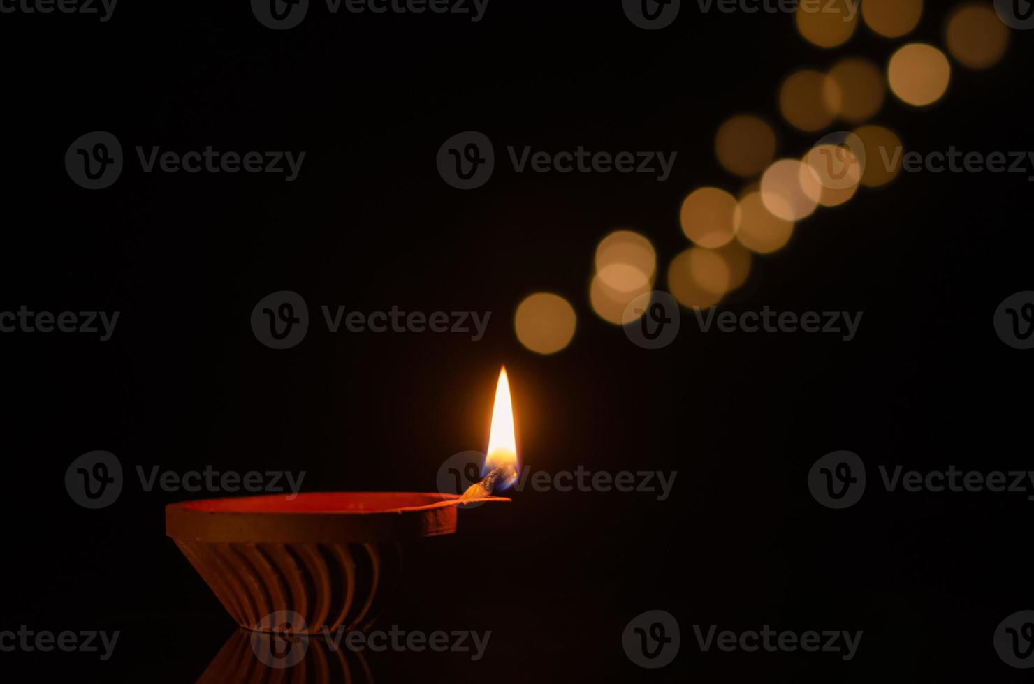 Selective focus on flame of clay diya lamp lit on dark background with bokeh lights. Diwali festival concept. photo