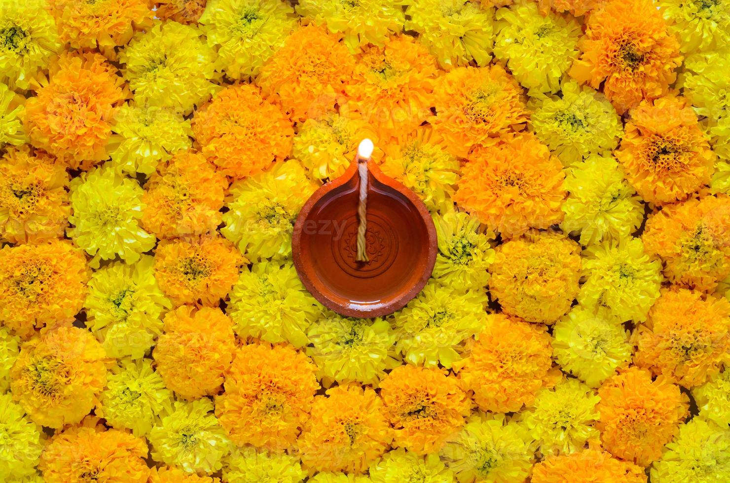 Decorative marigold flower rangoli for Diwali festival with clay diya lamp lit with blurred focus flame. photo