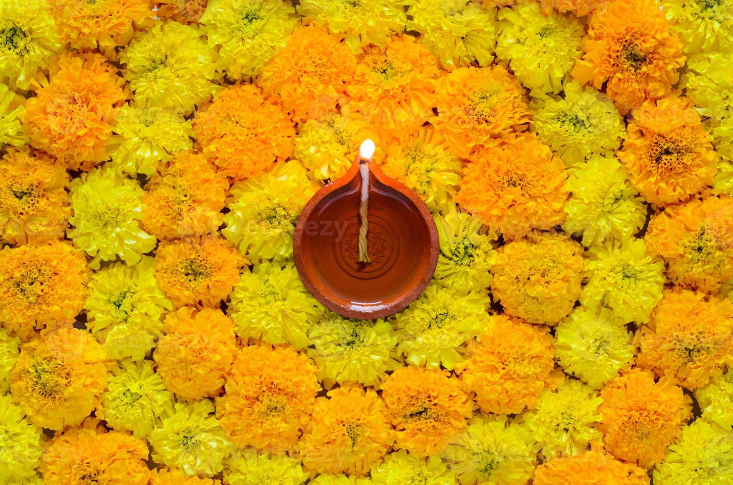 rangoli de flor de caléndula decorativa para el festival de diwali con lámpara diya de arcilla iluminada con llama de enfoque borrosa. foto