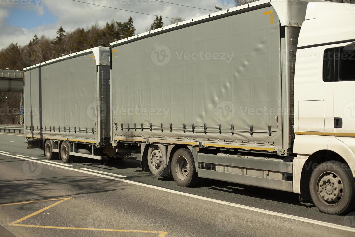 camión con carrocería gris y cabina blanca. camión en la carretera. conduciendo por la autopista. Transporte de carga. foto