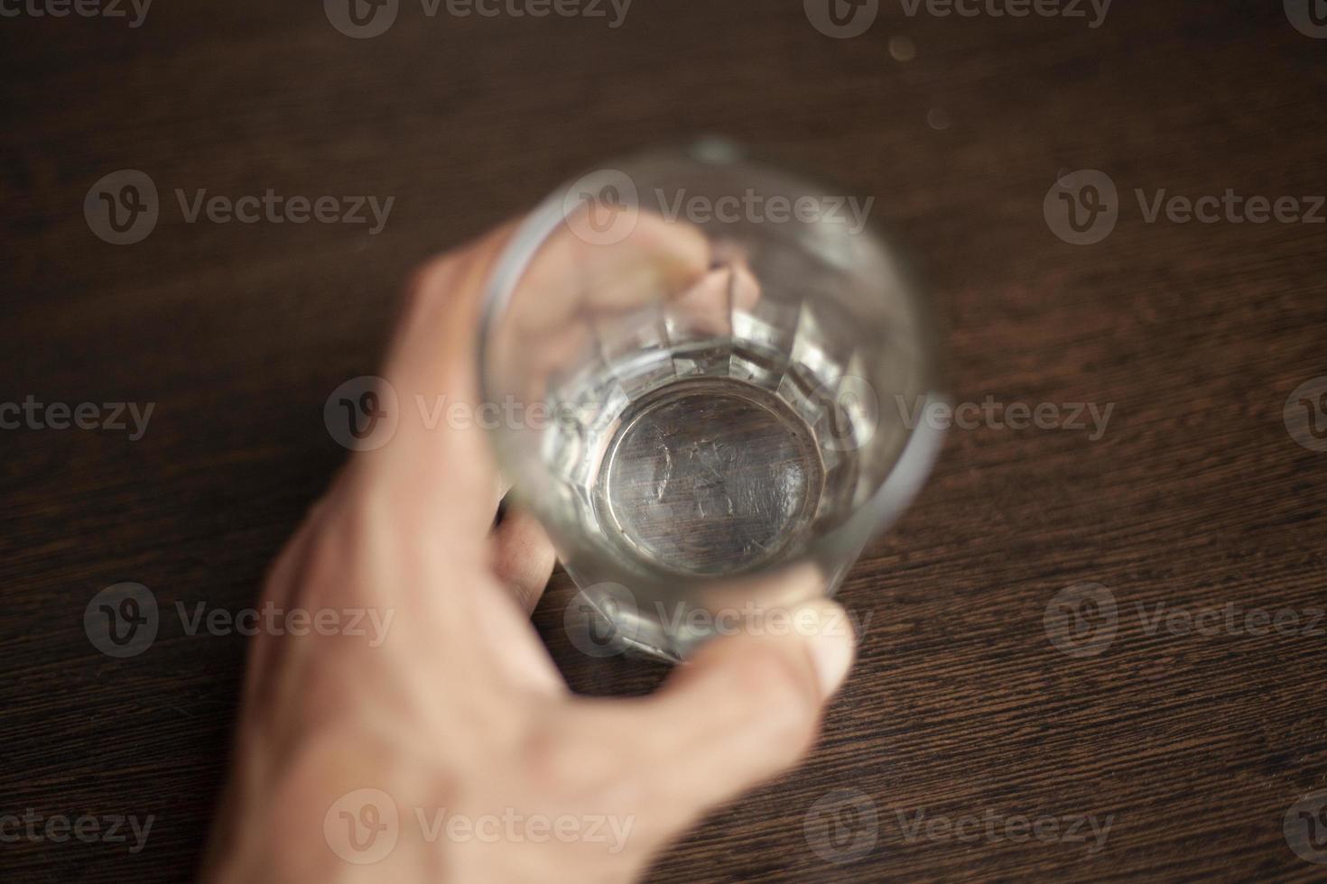 The bottom of an empty glass is in focus. Hand holds a glass mug. Capacity for liquid. photo