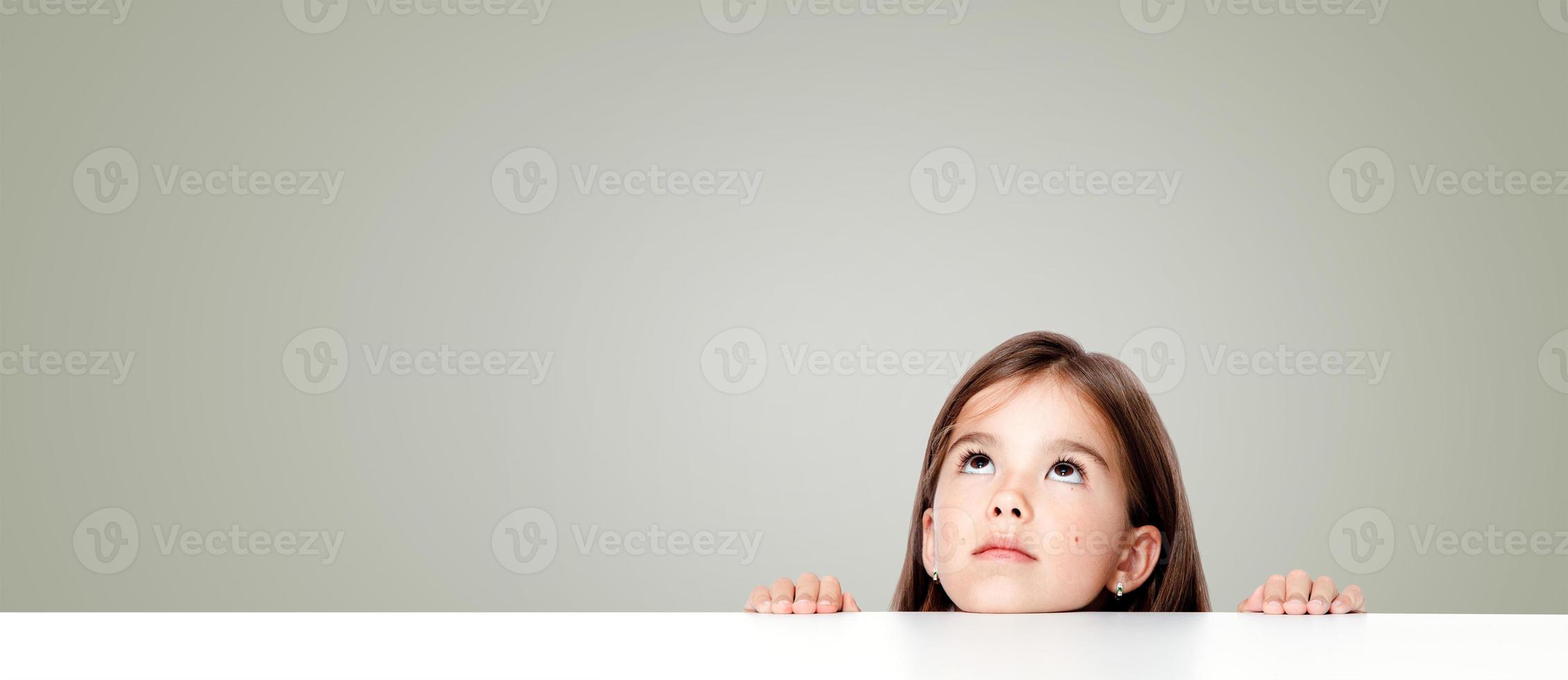 Cute little child girl looking up on the desk at school. photo