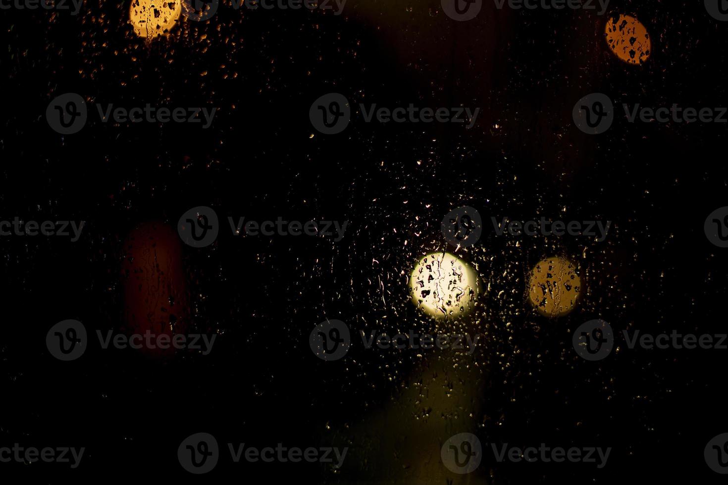 Raindrops on the glass. Blurry background with lights. The texture of the glass on a dark background. photo