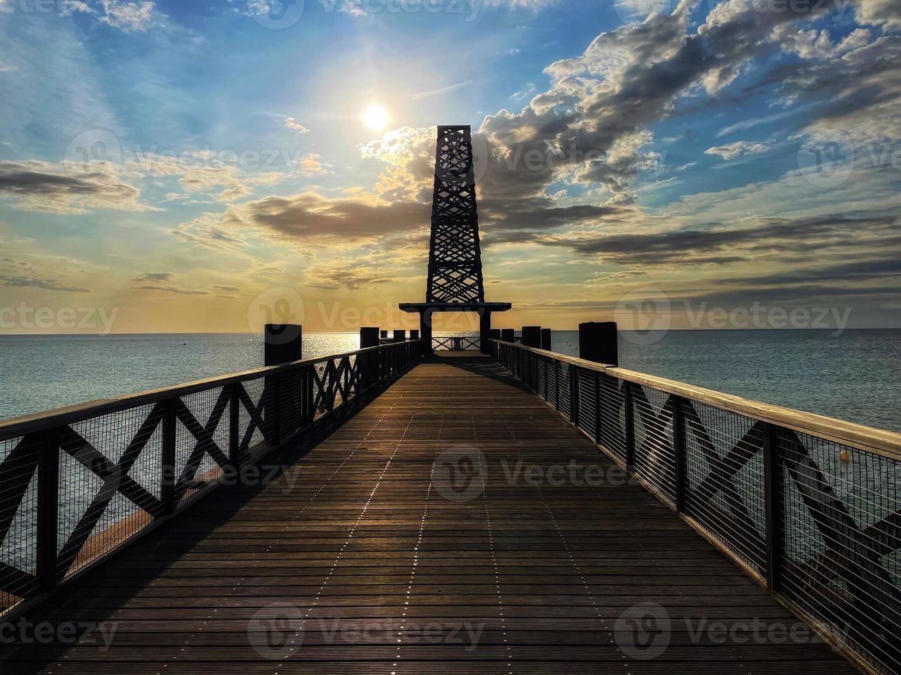 A wooden bridge on the beach leads to the sea at sunrise on a blue summer sky photo