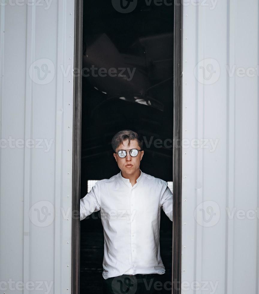 A handsome guy in sunglasses opens the door to the hangar. photo