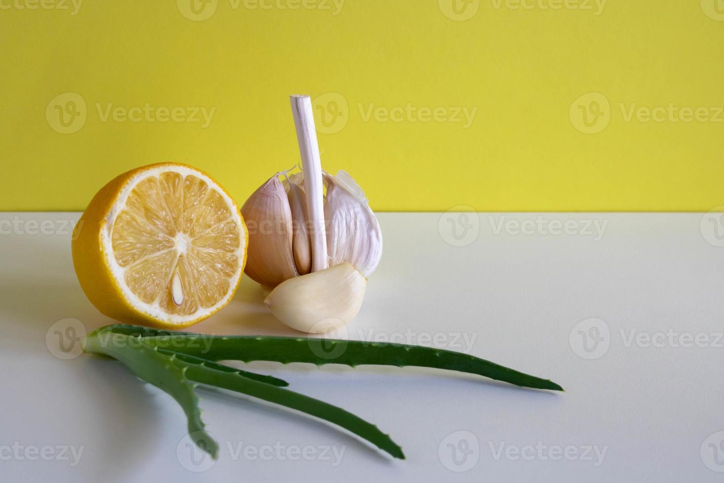 Composition with natural cold remedies on a white table on a yellow background. Garlic, lemon, aloe folk remedies against the autumn cold, covida. Space for text photo