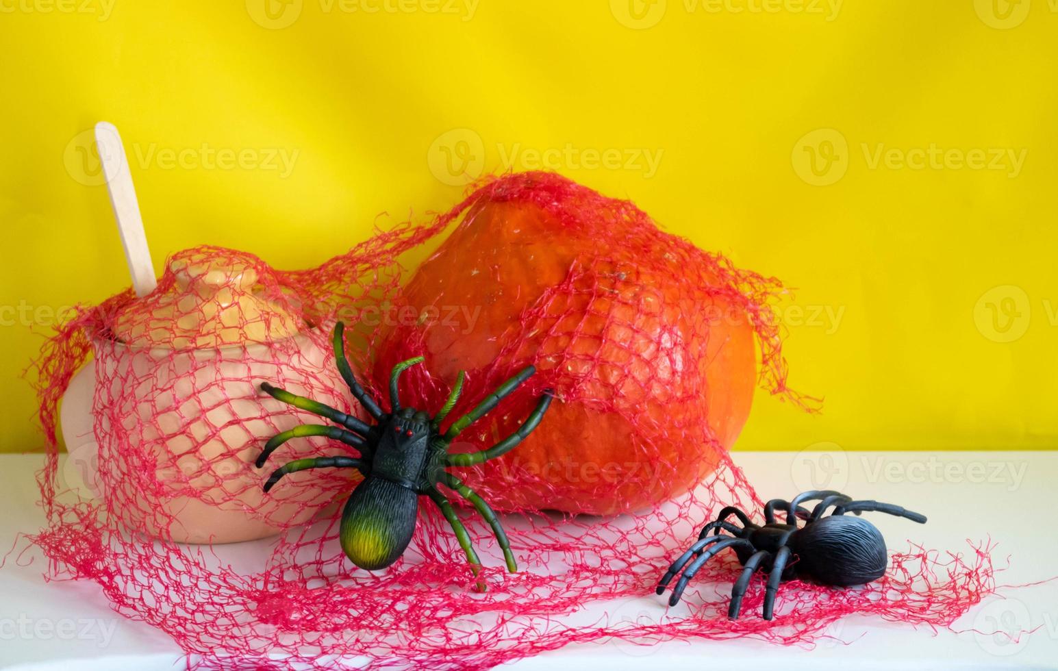 A clay pot with a wooden spoon, a pumpkin and two spiders with a red web on a white background.Halloween and Thanksgiving Day Concept photo