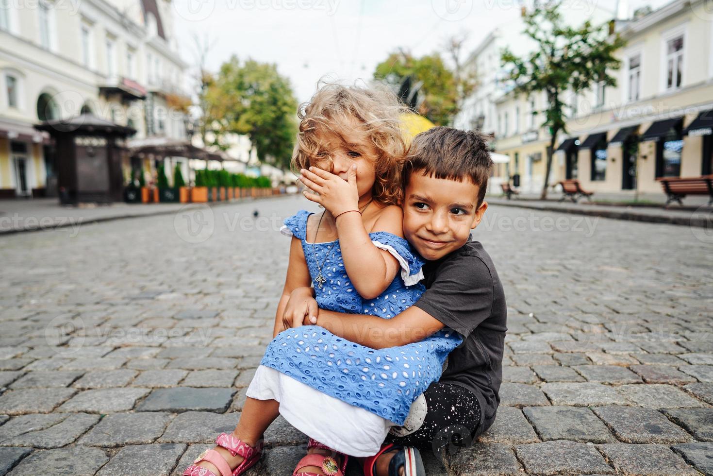 little boy and girl are sitting on the street photo
