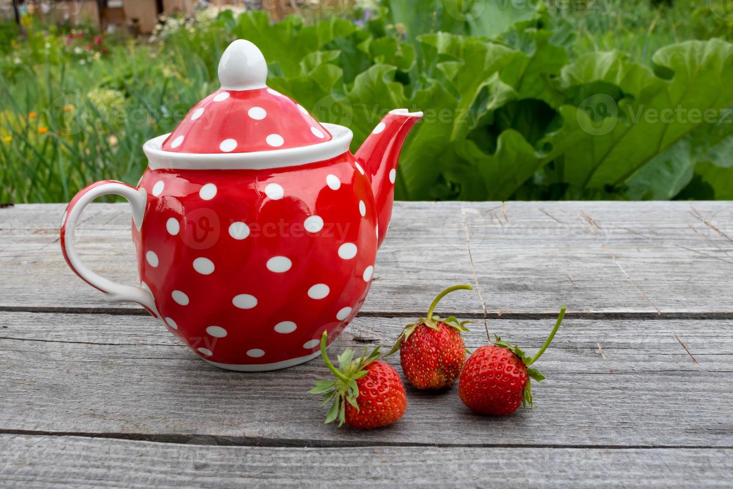Red vintage teapot with a polka dot pattern on a wooden background next to strawberries. Place for text photo