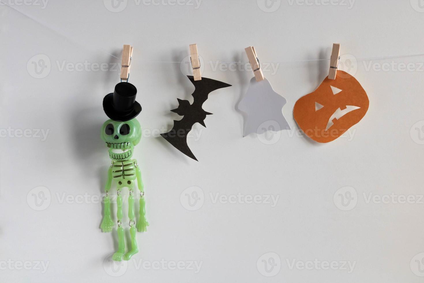 A toy skeleton in a top hat, a bat, a ghost and a pumpkin hang on clothespins. Halloween concept photo