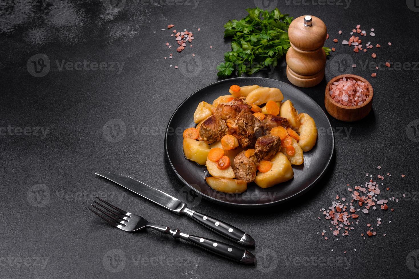 Beef meat and vegetables stew on a black plate with roasted potatoes photo
