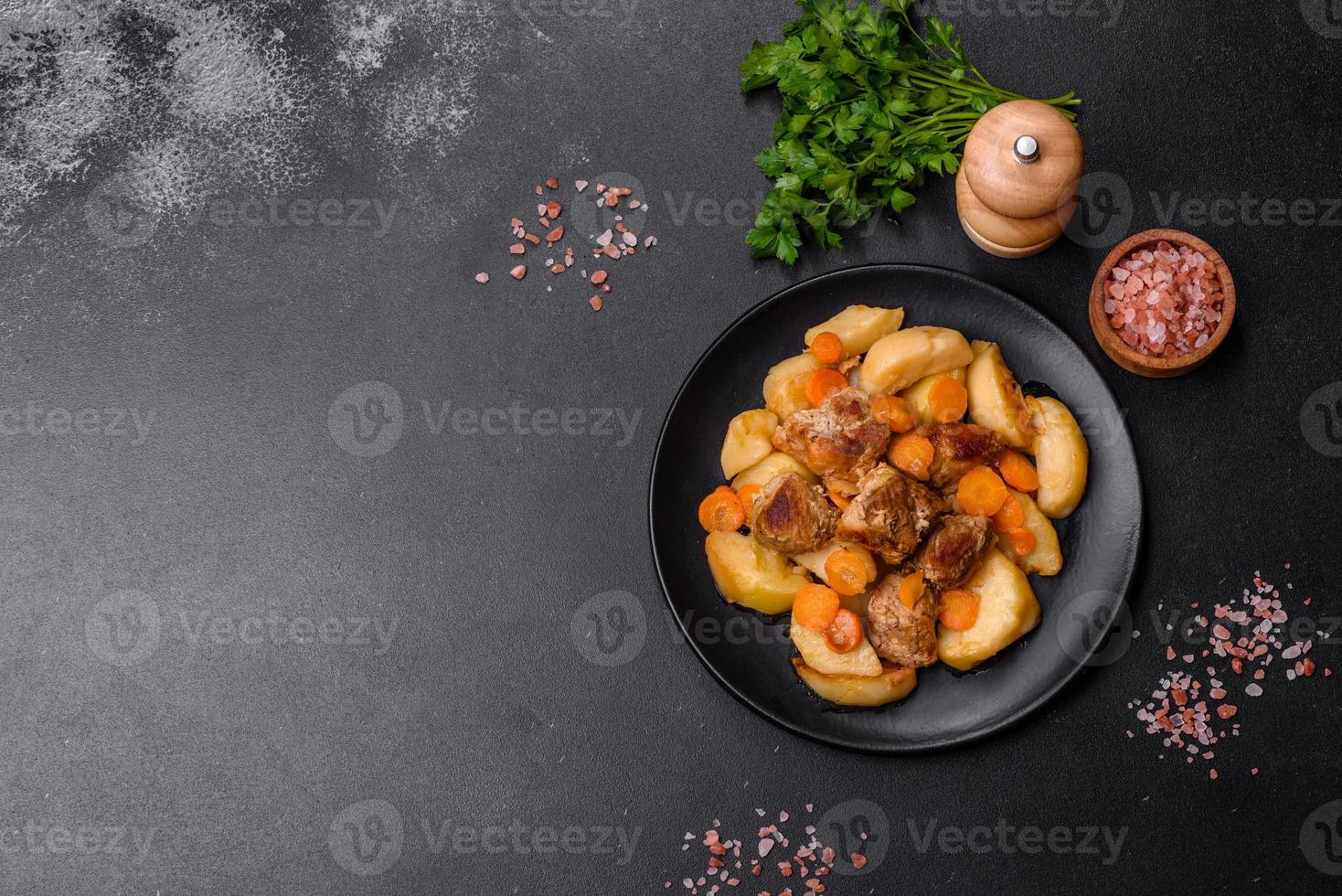 Beef meat and vegetables stew on a black plate with roasted potatoes photo