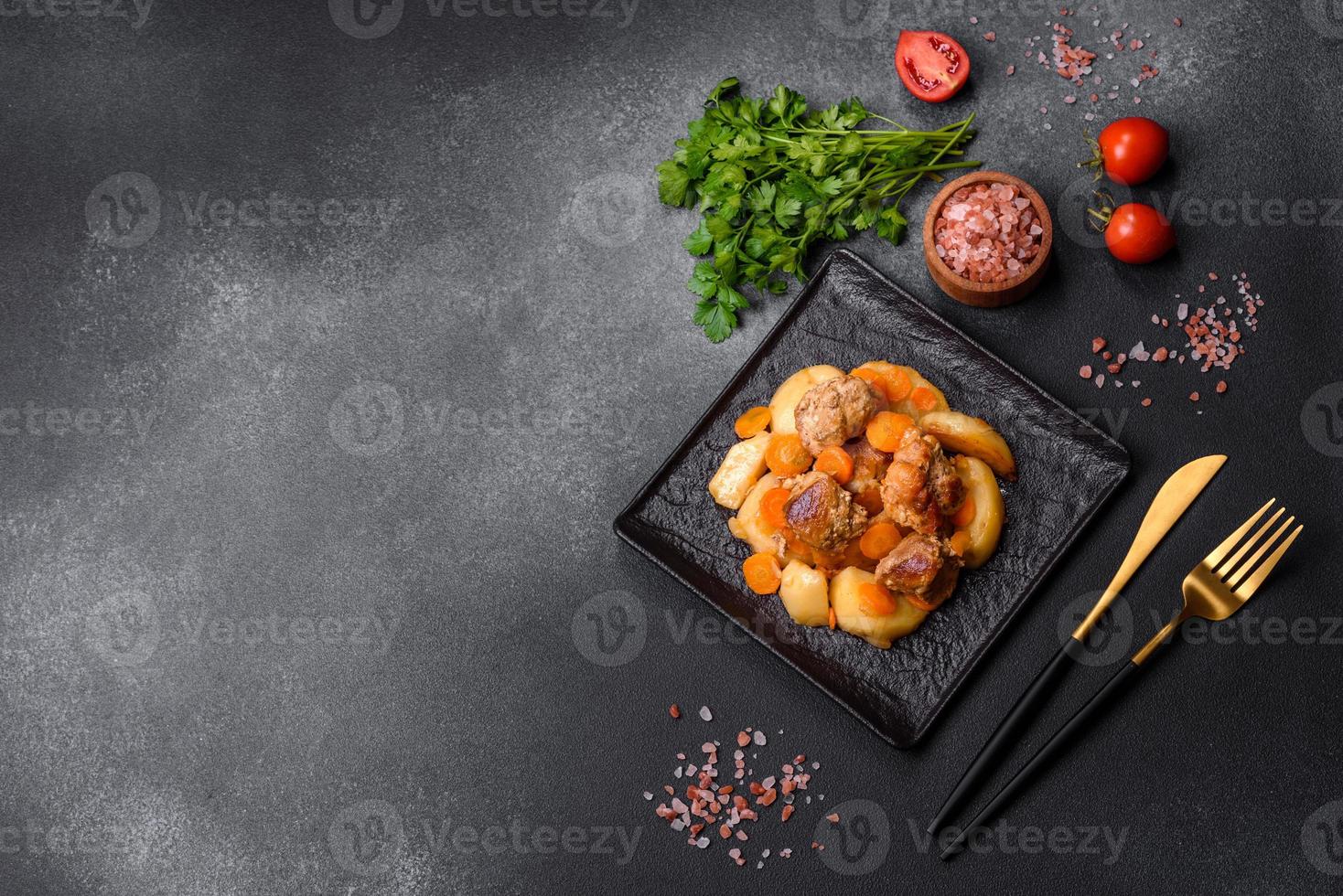 Beef meat and vegetables stew on a black plate with roasted potatoes photo