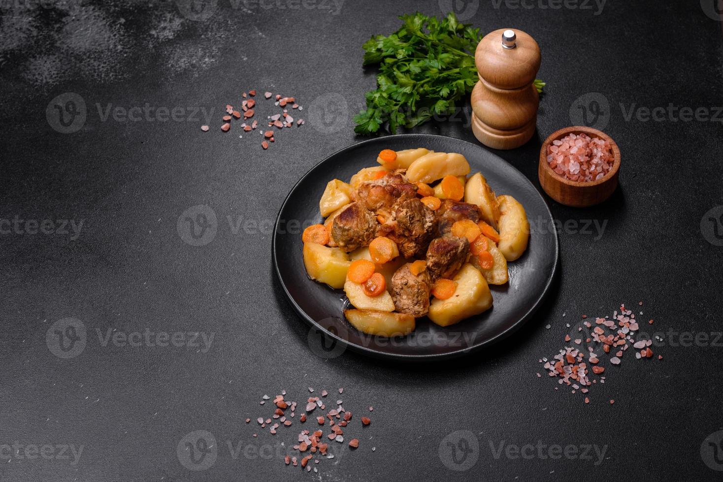 Beef meat and vegetables stew on a black plate with roasted potatoes photo