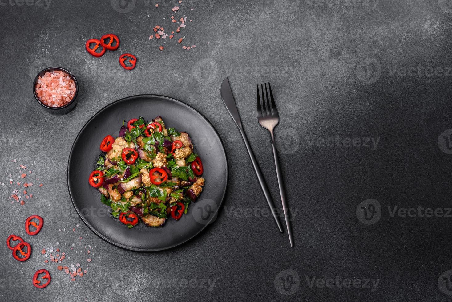 A salad of baked aubergine, sweet pepper, garlic, zucchini and parsley in a black plate photo