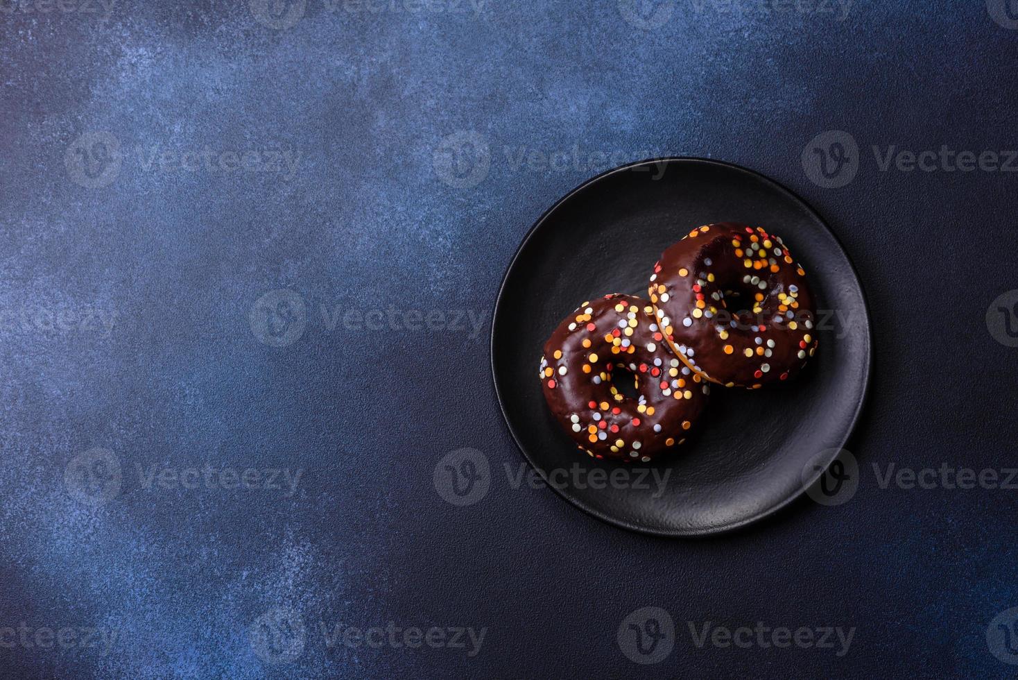 concepto de pasteles. donuts con glaseado de chocolate con chispas, sobre una mesa de hormigón oscuro foto