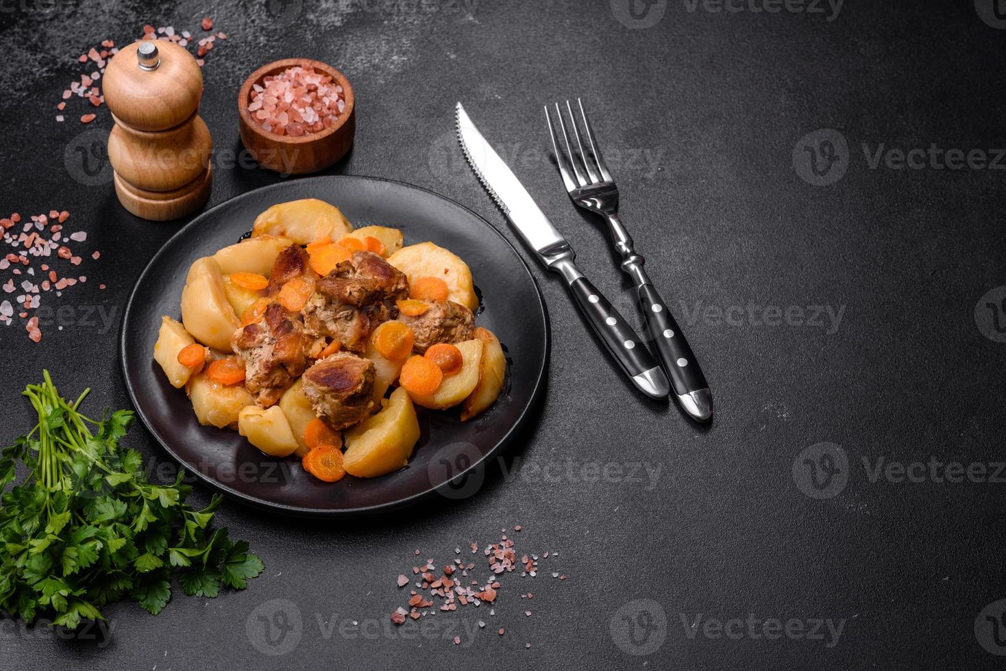 Beef meat and vegetables stew on a black plate with roasted potatoes photo