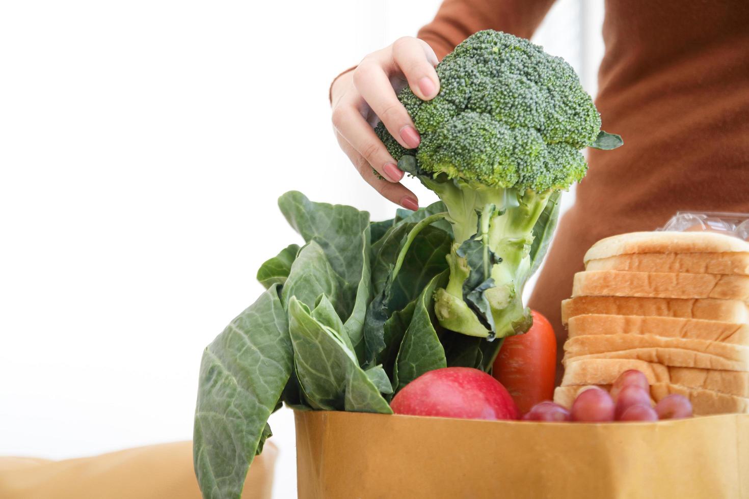 Young woman picks fresh vegetables from a brown paper bag. That order from online groceries Home delivery. photo