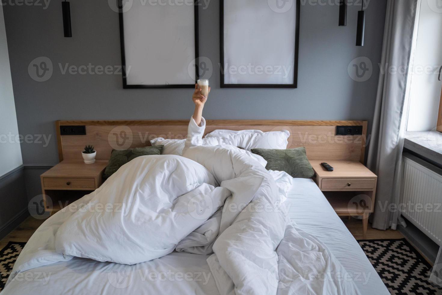 Hand holding a cup of coffee at home in bed photo