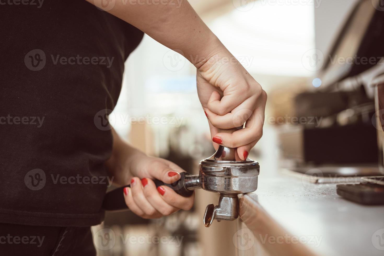 Barista presses ground coffee using tamper. Close-up view on hands photo