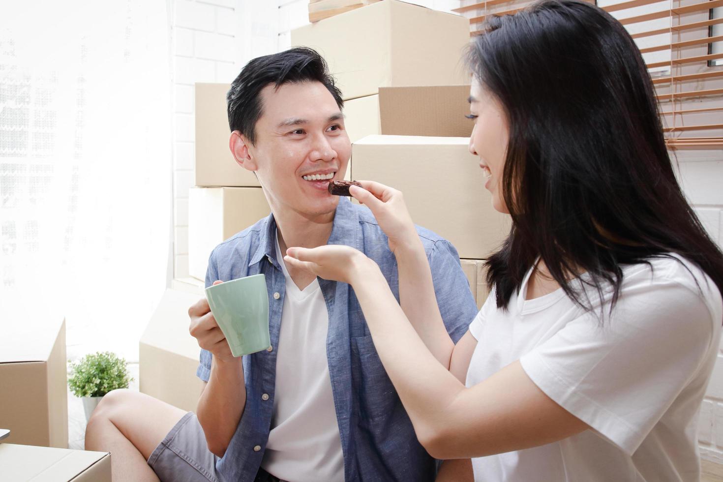 feliz pareja asiática sonriente mudándose a un nuevo hogar la esposa alimenta a su marido con bocadillos. concepto de familia, el comienzo de una nueva vida. foto