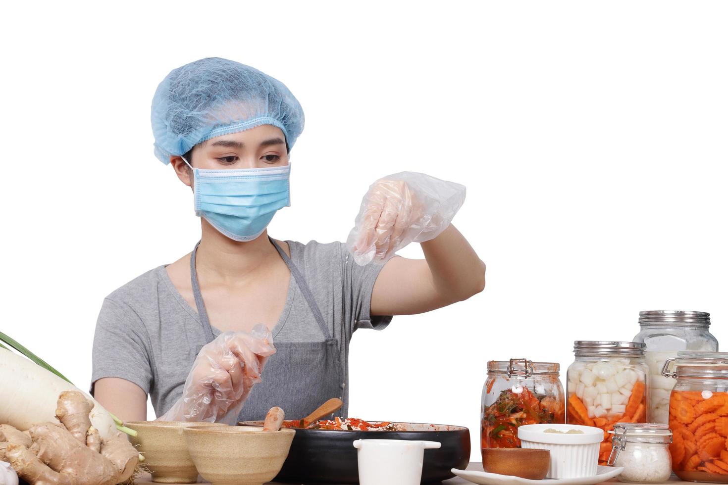 mujer asiática sentada y haciendo kimchi usa una máscara, guantes y una gorra protectora para mantener la comida limpia. Fondo blanco. concepto de comida fermentada coreana hecha de vegetales. camino de recortes aislado foto