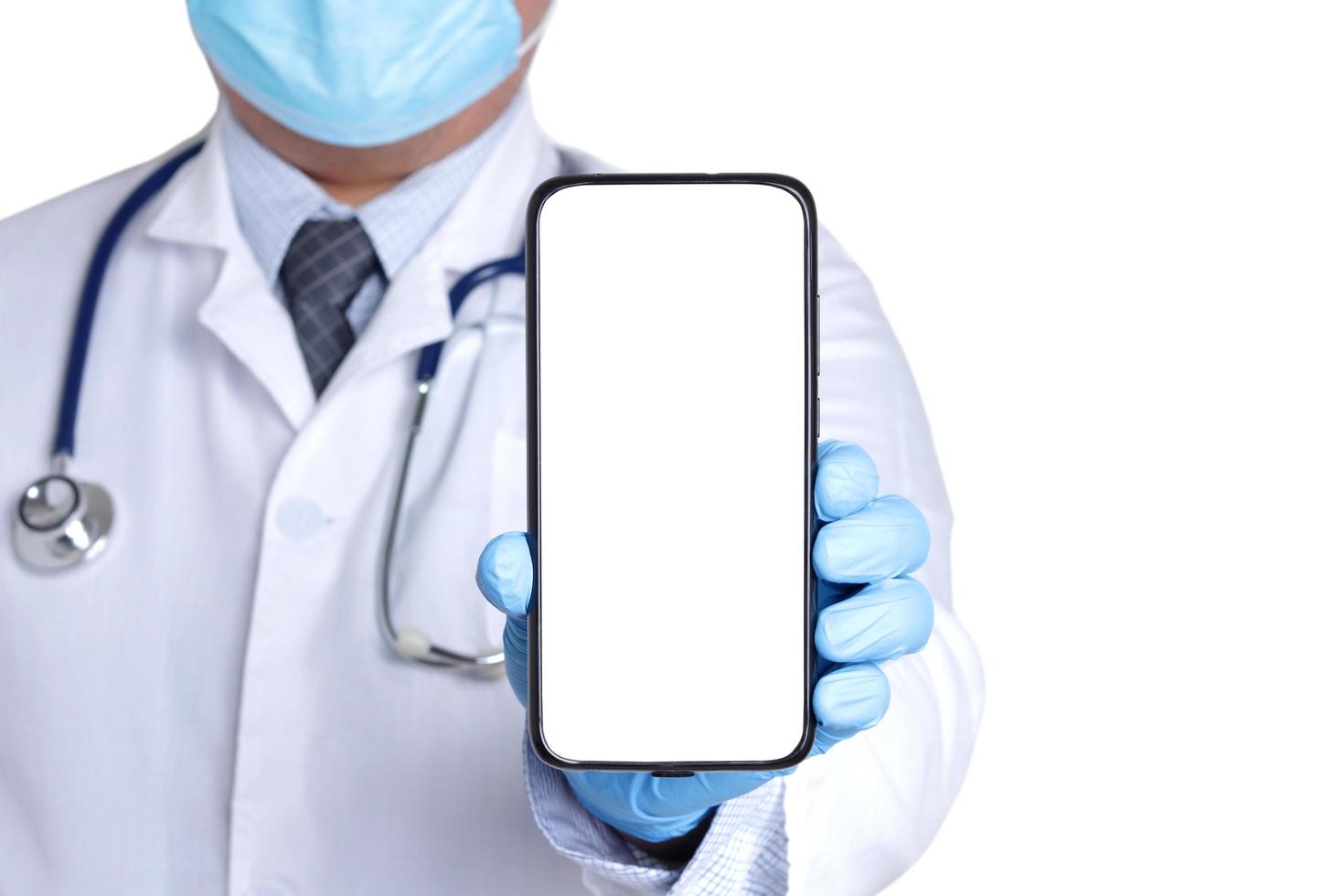 médico con mascarilla quirúrgica y guantes azules. sostenga el teléfono inteligente con una pantalla blanca. conectarse a la comunicación a través de la tecnología en línea. los médicos pueden examinar a los pacientes a través de videollamadas. foto