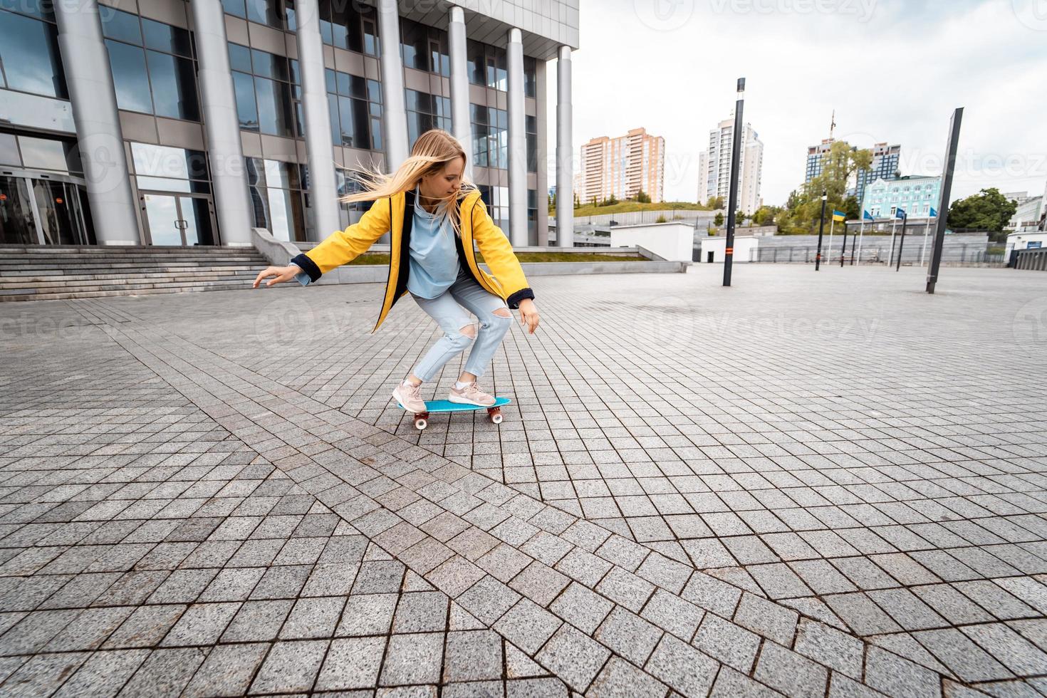 Blond female hipster woman riding on the longboard in the street at city. photo