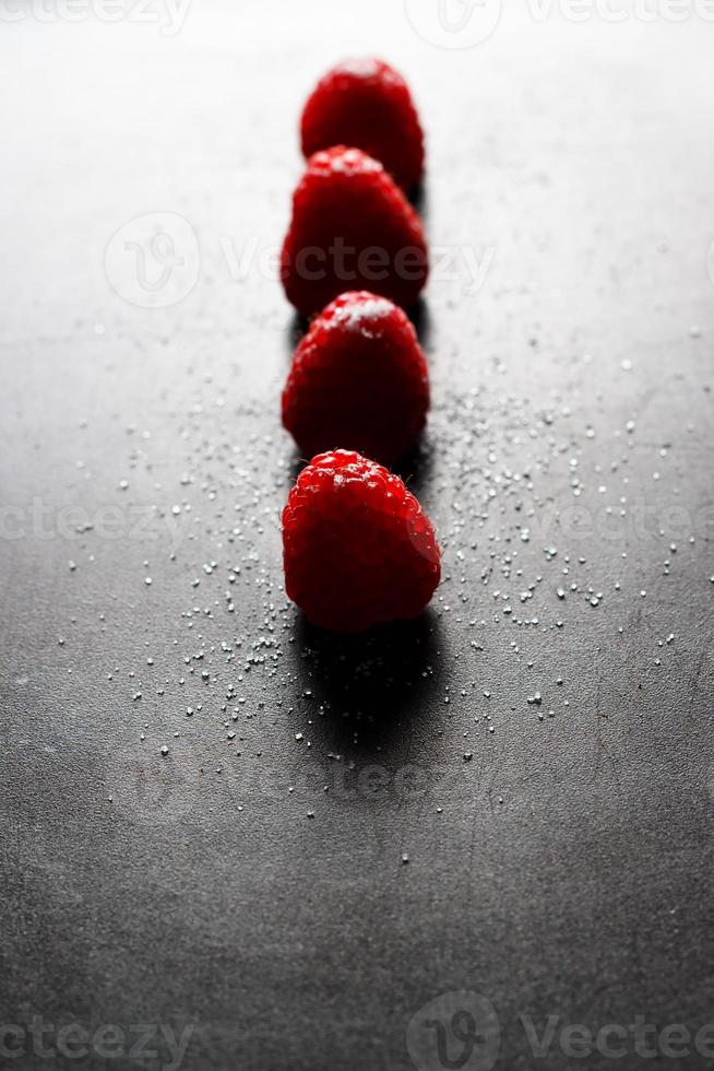 Red raspberries in a row with sugar on top on a black griddle. Backlighting. Vertical image. photo