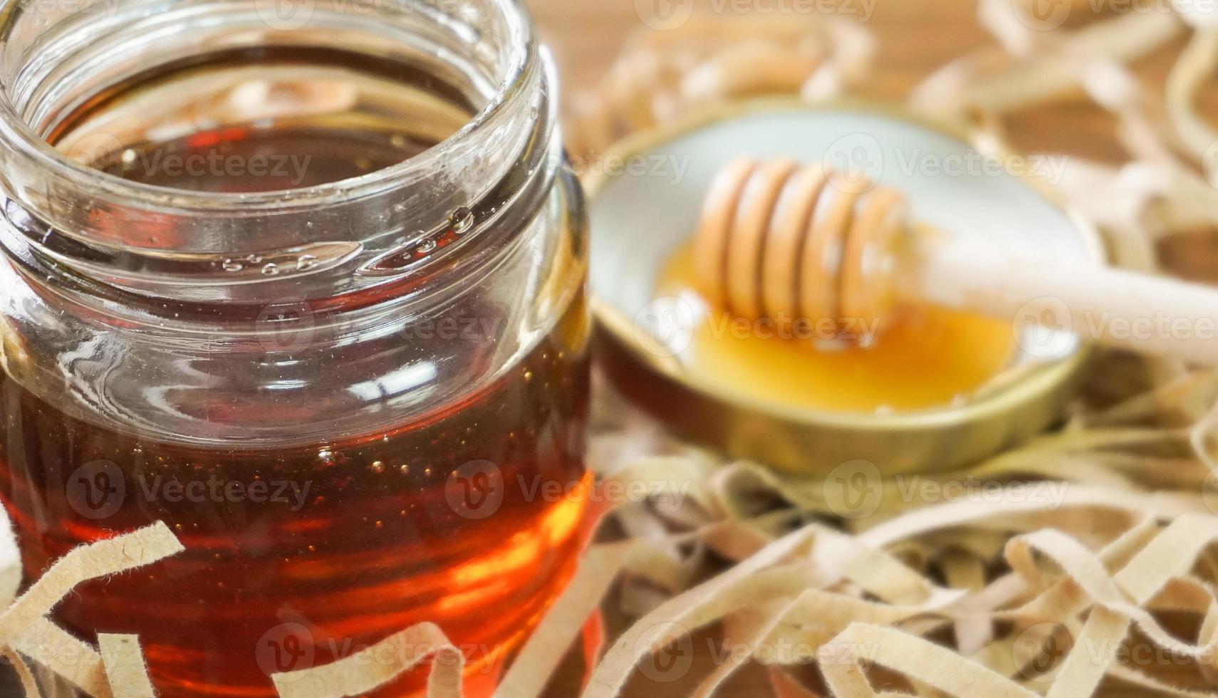 Honey in glass jar with blurred honey dipper in background. Health and beauty product sustainable lifestyle concept. photo