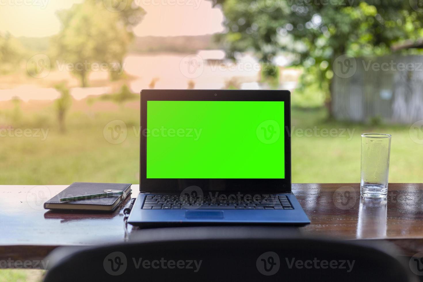 Green screen notebook with notebooks placed on a wooden table against a beautiful natural scenery background. photo