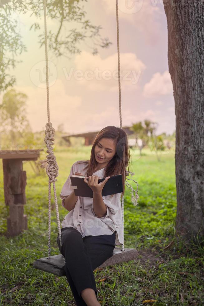 A beautiful woman sits on a swing and writes down something in a notebook with love. photo