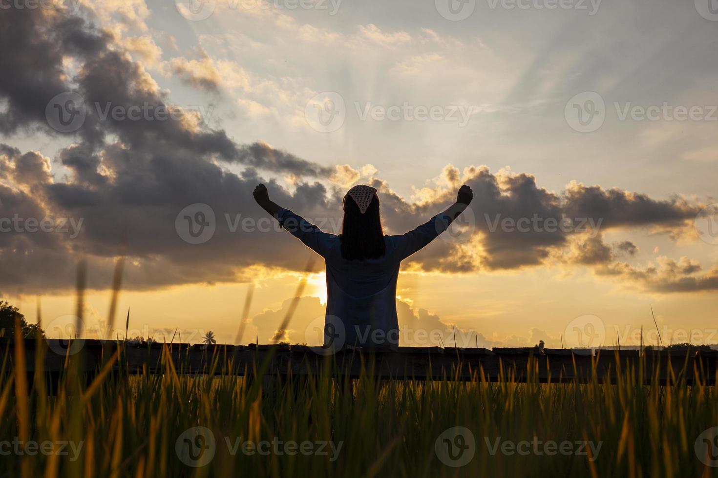 Behind the shadow of a woman sitting on a wooden walkway beside a field. waving joyfully in the setting sun photo