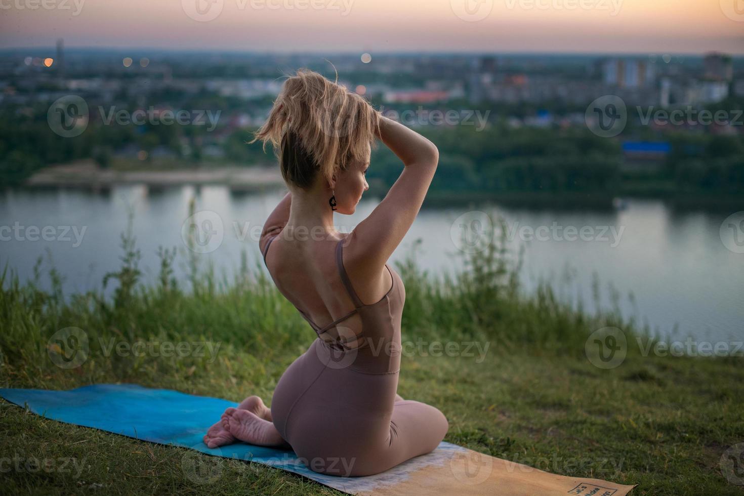 una joven gimnasta hace yoga en la naturaleza en un parque contra el cielo, usando una combinación de posturas de yoga tradicionales, pilates y danza suave. conexión con la naturaleza. foto