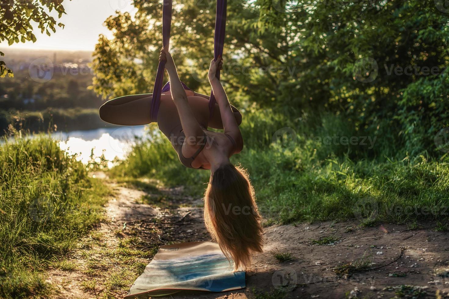 A young gymnast is engaged in aerial yoga in nature in the park, using a combination of traditional yoga poses, pilates and gentle dance photo