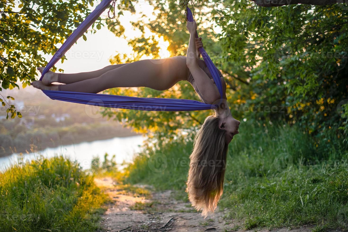 A young gymnast is engaged in aerial yoga in nature in the park, using a combination of traditional yoga poses, pilates and gentle dance photo