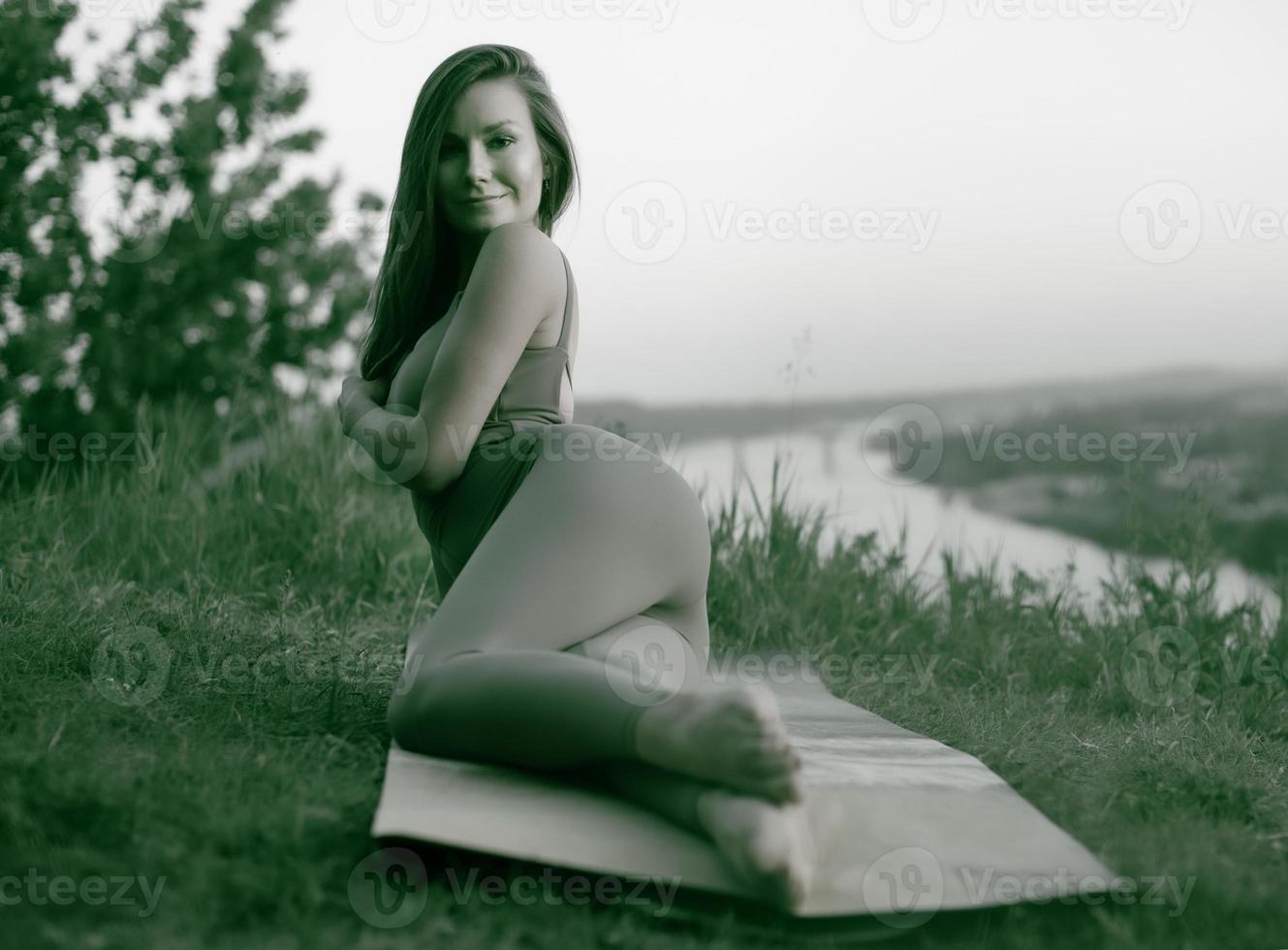 una joven gimnasta hace yoga en la naturaleza en el parque, usando una combinación de posturas de yoga tradicionales, pilates y danza suave. conexión con la naturaleza. foto