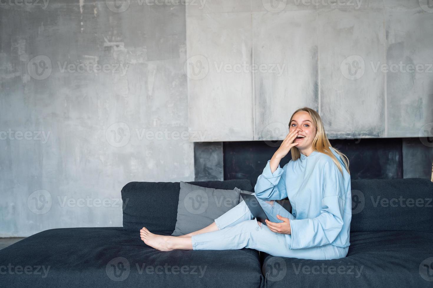 Image of happy woman using silver laptop while sitting on sofa photo