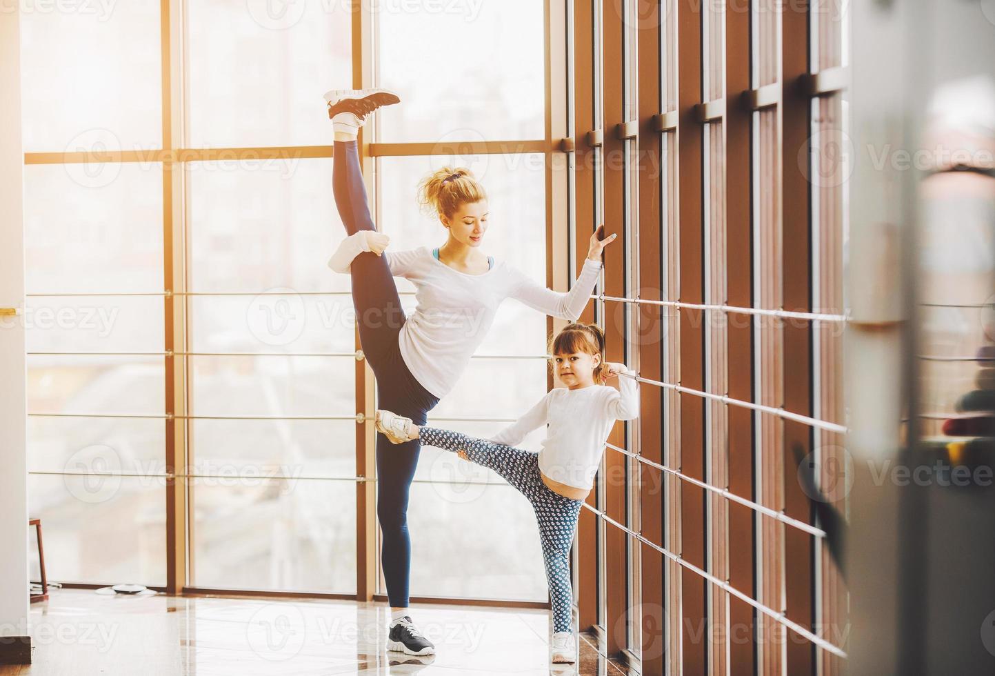 madre aprendiendo a hija a hacer un estiramiento alto de piernas foto