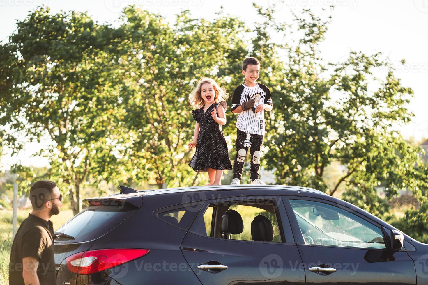 Two children stand on the roof of a car photo