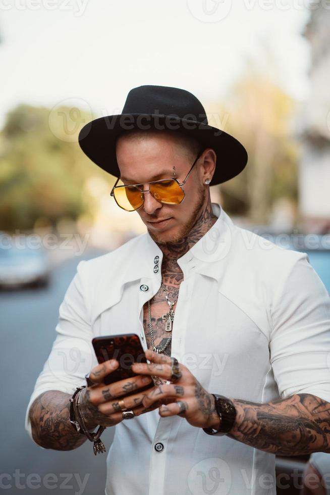 A young man in a hat and sunglasses holds a mobile phone in his hands photo