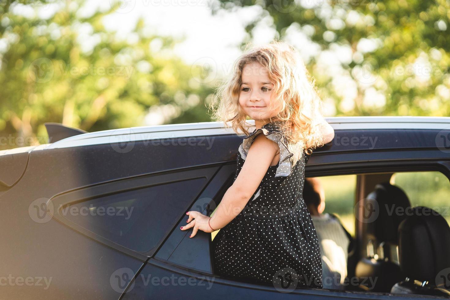 A little girl is sitting on the door of the car photo